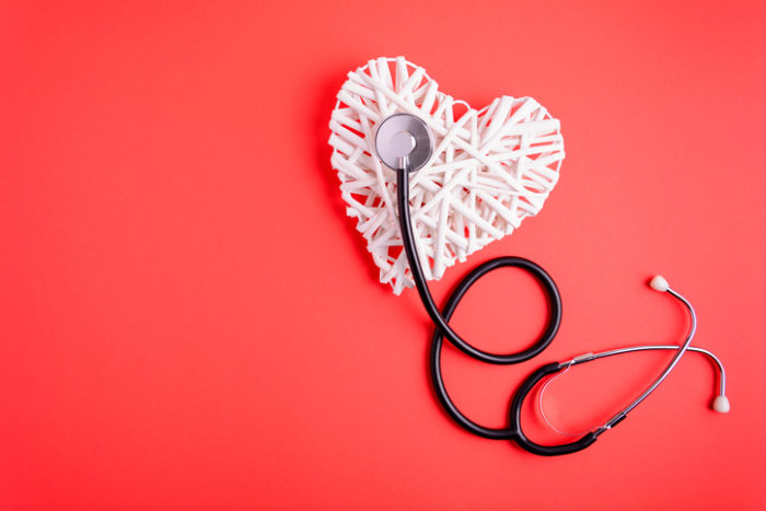 White wooden heart with black stethoscope on red paper background